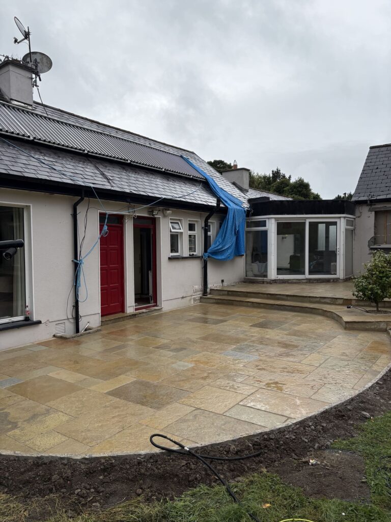 Renovated patio with stone tiles, red door, and blue tarp, set against a cloudy sky in Wicklow. Driveways Wicklow featured