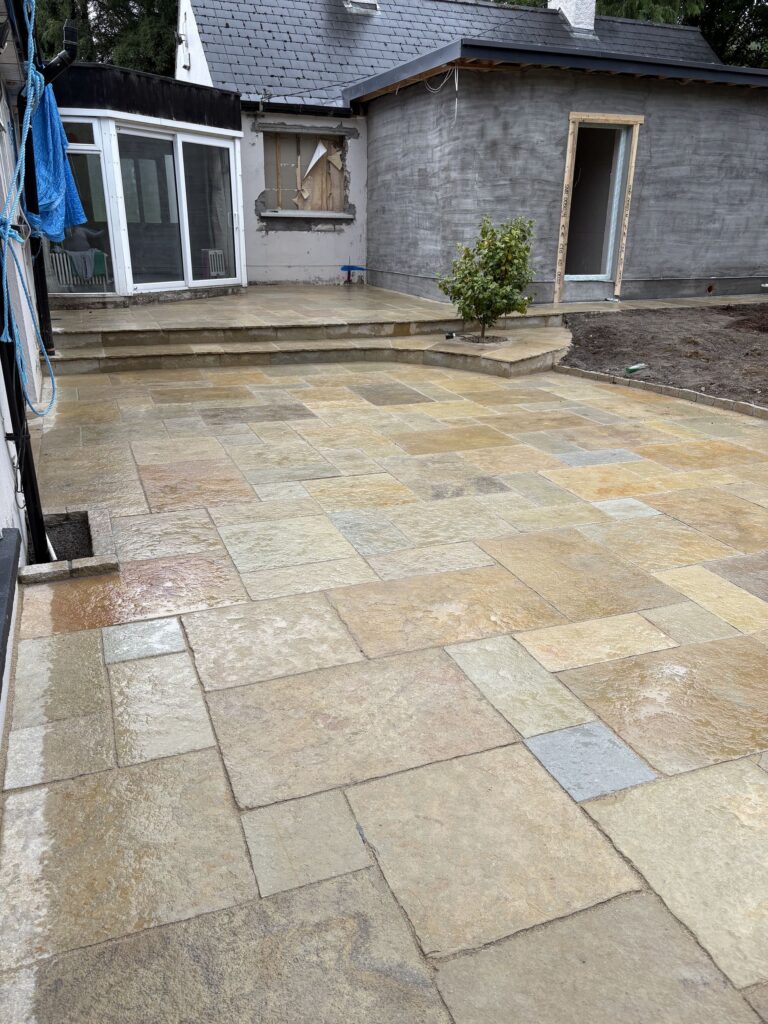 Newly paved driveway with large stone slabs, wet from rain, adjacent to a house under renovation in Wicklow