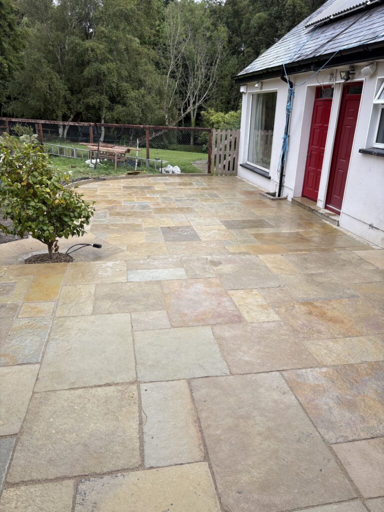 Paved patio area with large stone tiles, two red doors, and a green garden backdrop in Wicklow