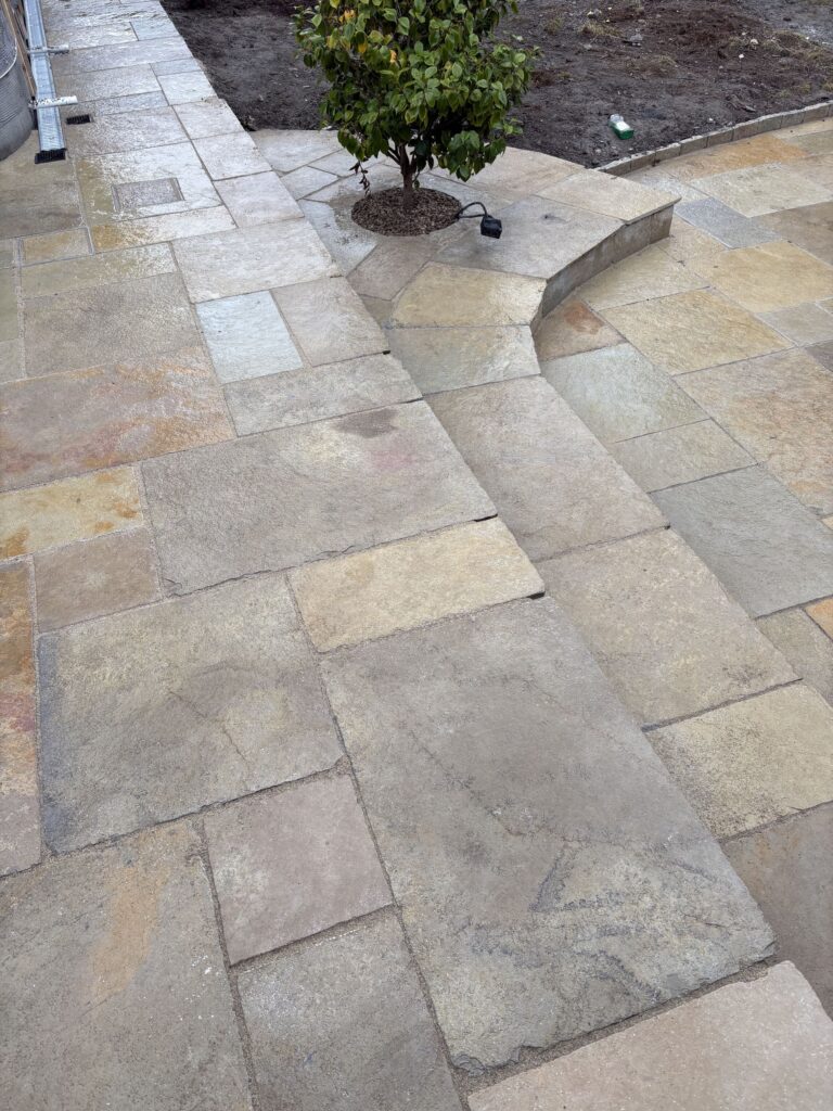 Sandstone patio with various shades of beige and brown, featuring a small bush and a slight incline in Wicklow