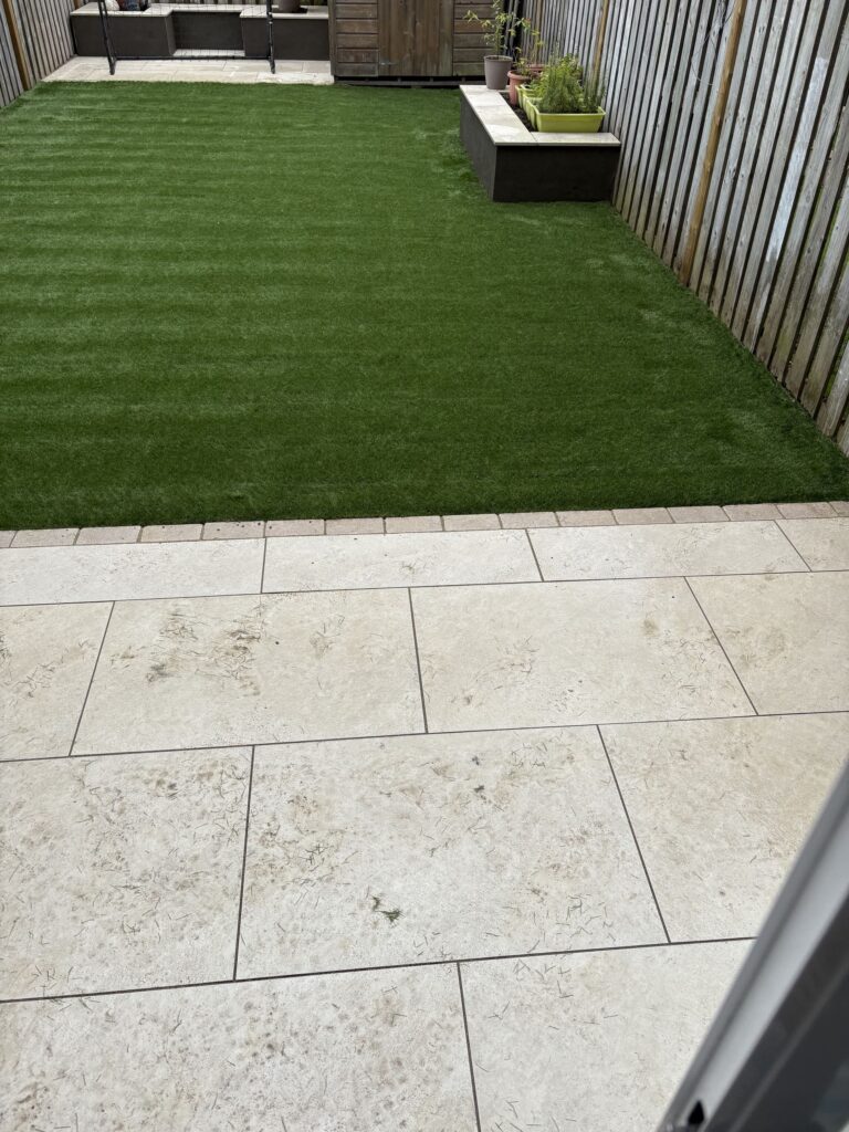 Light-colored sandstone patio with a green artificial lawn and wooden fence, showcasing a modern outdoor space in Wicklow