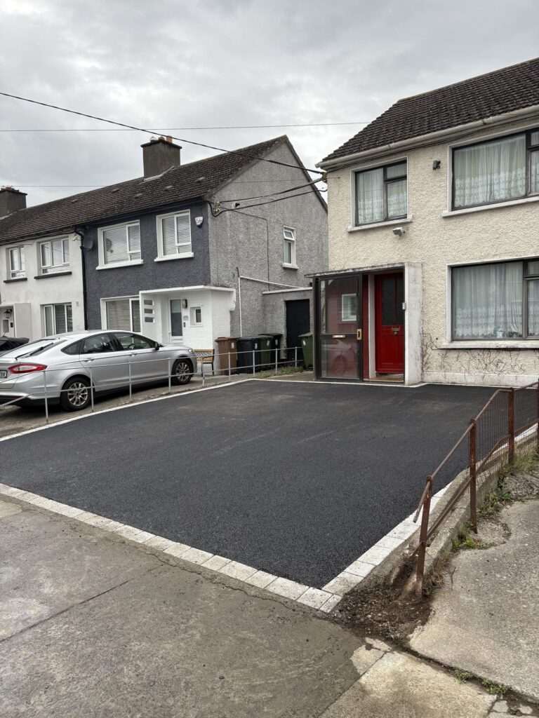 Newly paved black driveway with a white border, adjacent to two residential houses in Wicklow, under a cloudy sky