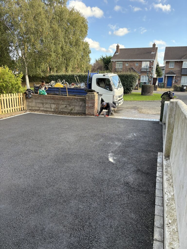 Workers laying a new black driveway in Wicklow, with a truck and residential homes in the background