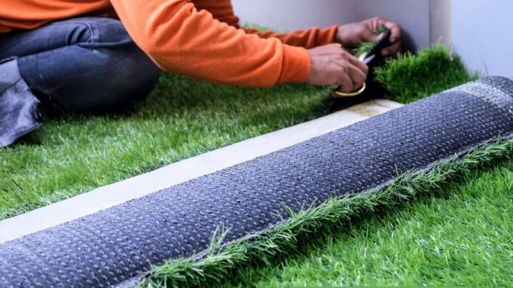 A person in an orange shirt lays artificial grass on a green surface, preparing it for installation in Driveways Wicklow