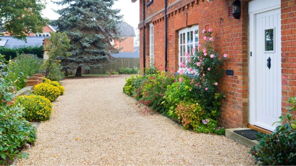 Gravel driveway lined with colorful flowers and shrubs, leading to a brick house with a white door in Wicklow