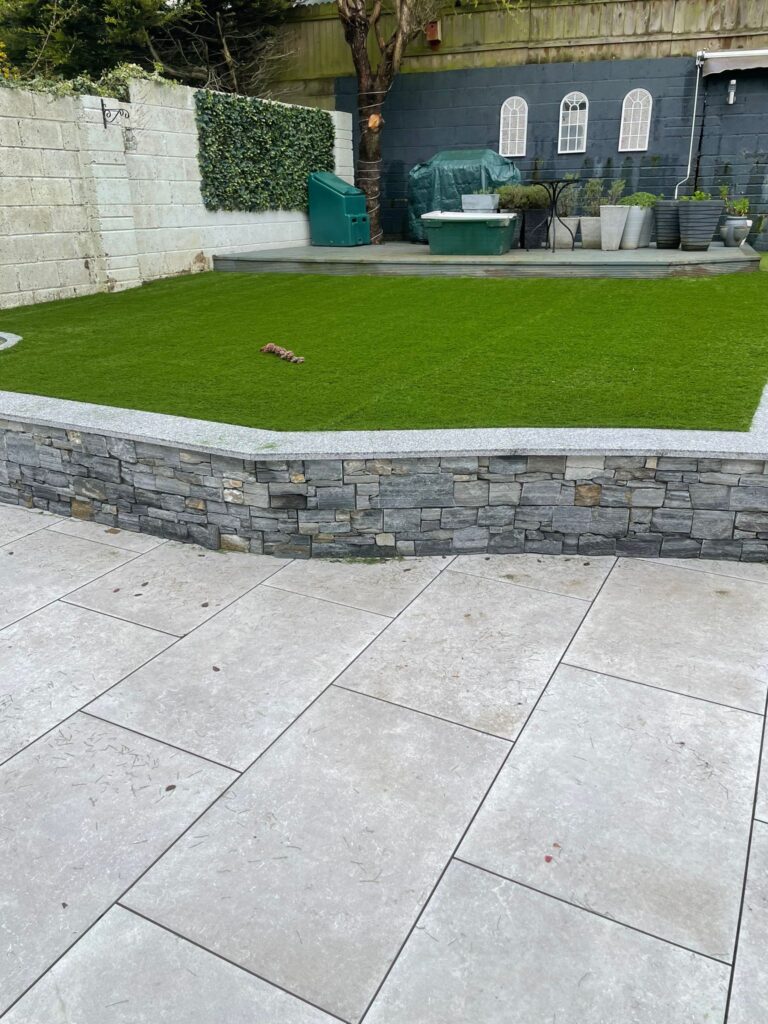 Lush green artificial grass surrounded by a stone wall, with a patio area and garden furniture in a Wicklow setting
