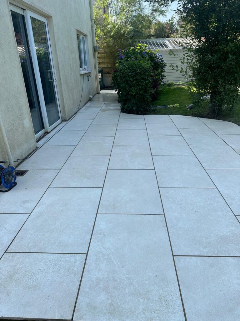 Light-colored sandstone patio with large tiles, surrounded by greenery and a house wall, showcasing Sandstone Patios Wicklow