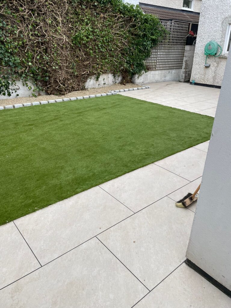 Lush green artificial grass contrasts with light sandstone patio tiles in a tidy outdoor space in Wicklow