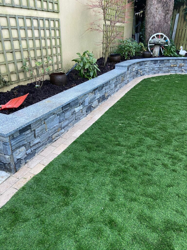 Lush green artificial grass, stone wall, and garden plants create a serene outdoor space in Landscaping Wicklow
