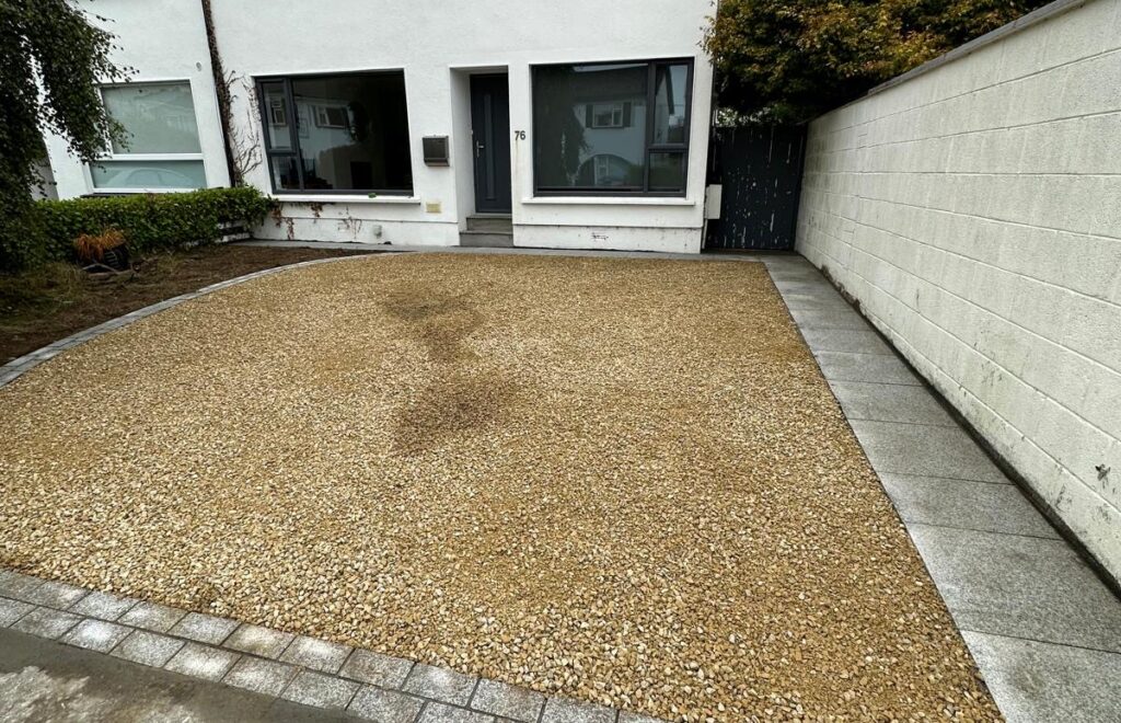 Gravel driveway with a stone border in front of a modern white house, featuring large windows and a dark door