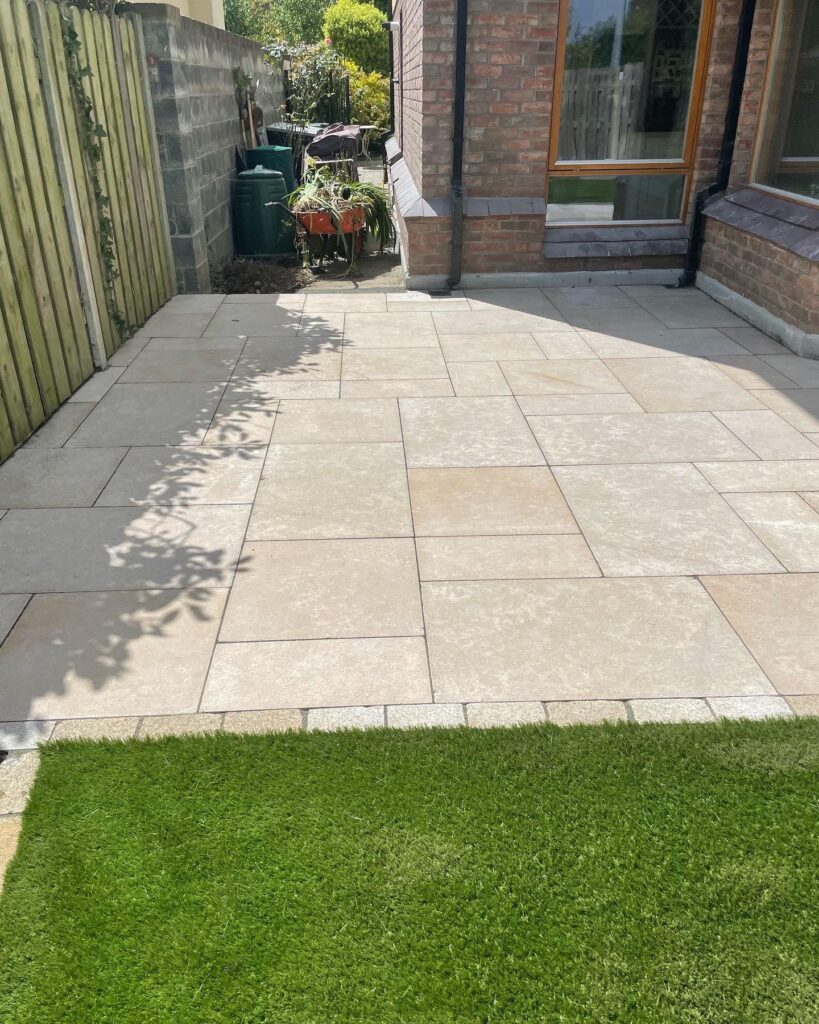 Paved patio area with light-colored stones, green grass, and a brick wall, showcasing driveway paving in Wicklow
