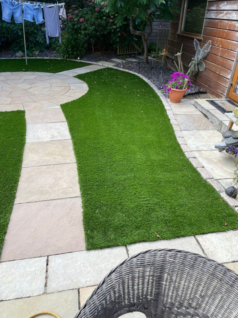 Lush green artificial lawn with stone pathway, potted flowers, and clothes drying on a line in a landscaped Wicklow garden