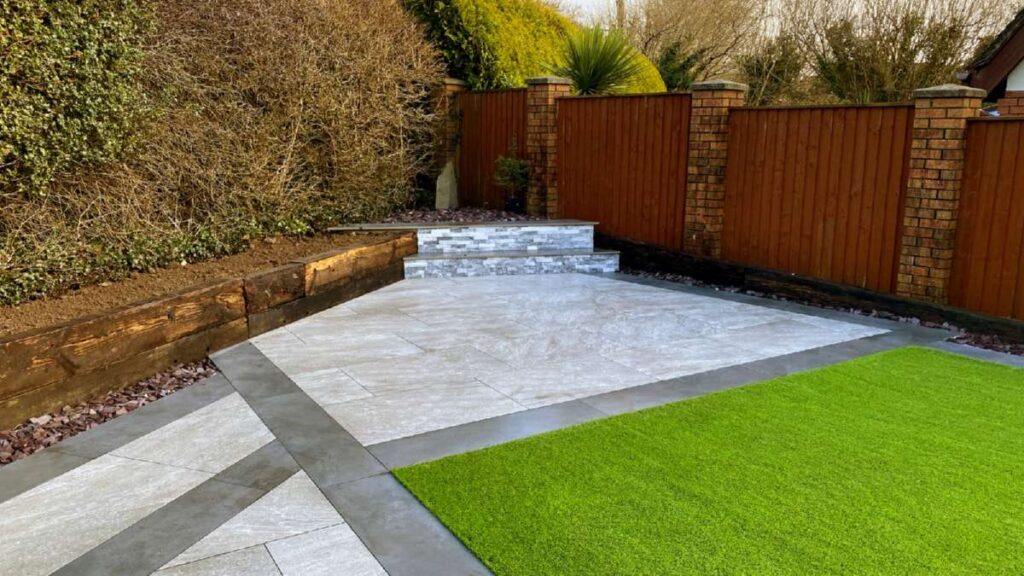 Stylish patio with gray tiles, green artificial grass, and stone steps, surrounded by wooden fencing and hedges in Wicklow