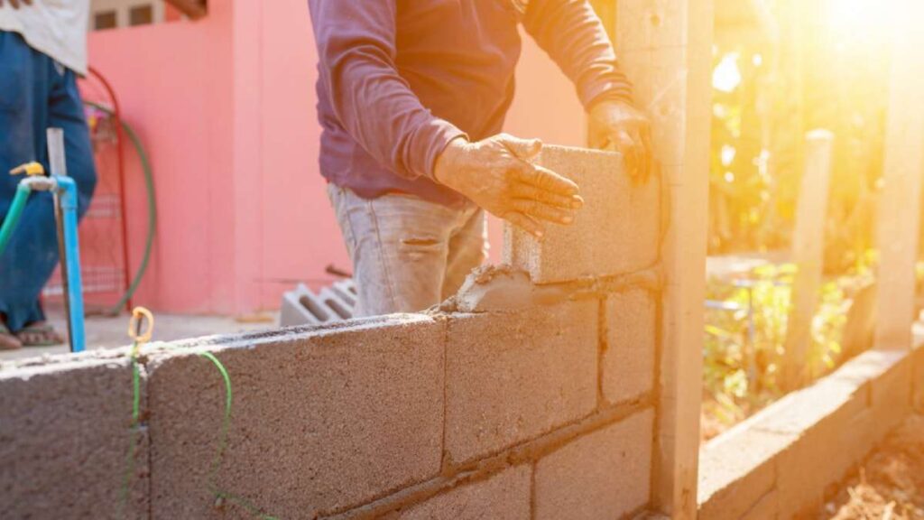 A worker lays concrete blocks in sunlight, constructing a wall near a pink building, showcasing Driveways Wicklow services