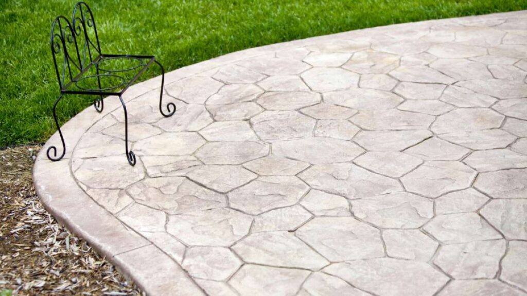 Curved patio with hexagonal stone pattern, featuring a small black metal chair and lush green grass in the background