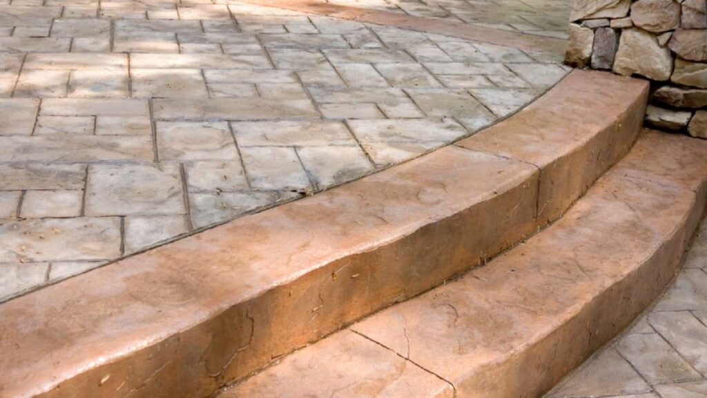 Textured sandstone patio with curved steps, showcasing warm earth tones and a natural stone wall in the background