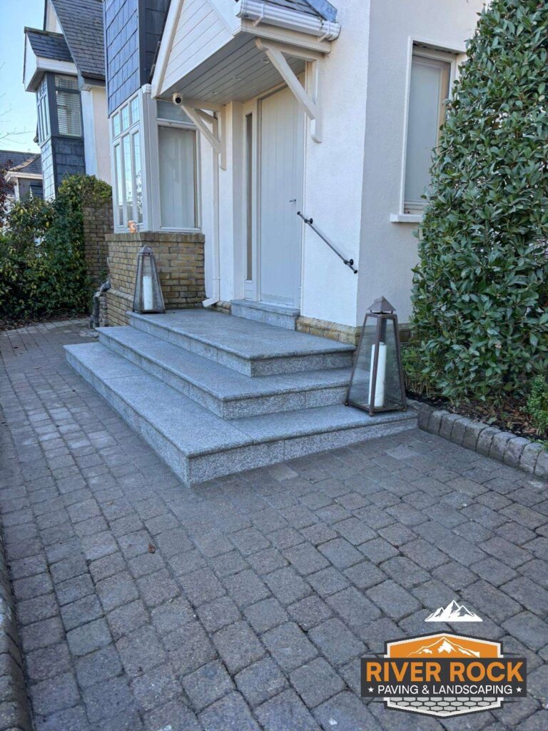Gray stone steps lead to a white front door, surrounded by greenery and a paved driveway, showcasing Driveway Paving Wicklow