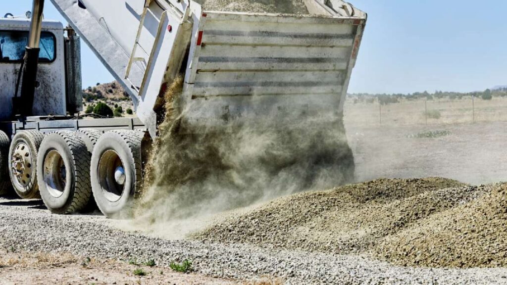 A dump truck unloads gravel on a construction site, creating a dust cloud, highlighting Gravel Driveways Wicklow