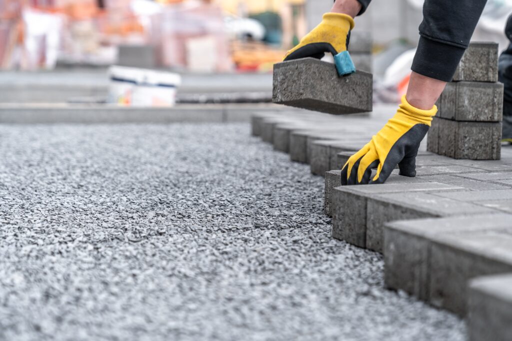 Worker in yellow gloves placing concrete blocks on a gravel surface, part of driveway installation in Wicklow
