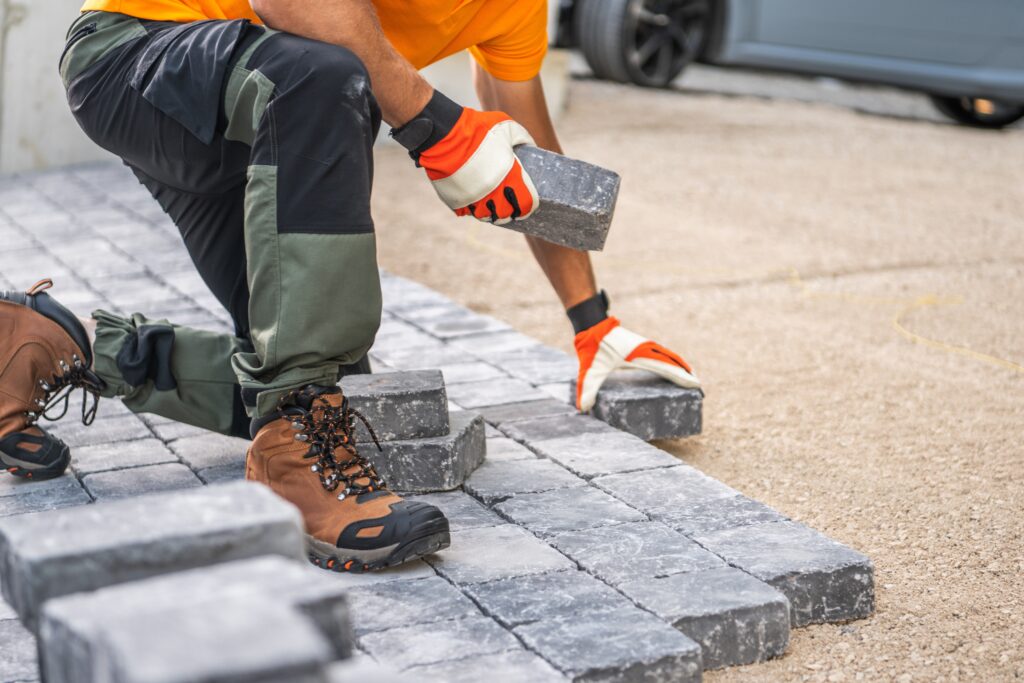 A worker in orange shirt and gloves lays gray paving stones on a driveway in Wicklow, kneeling on the ground