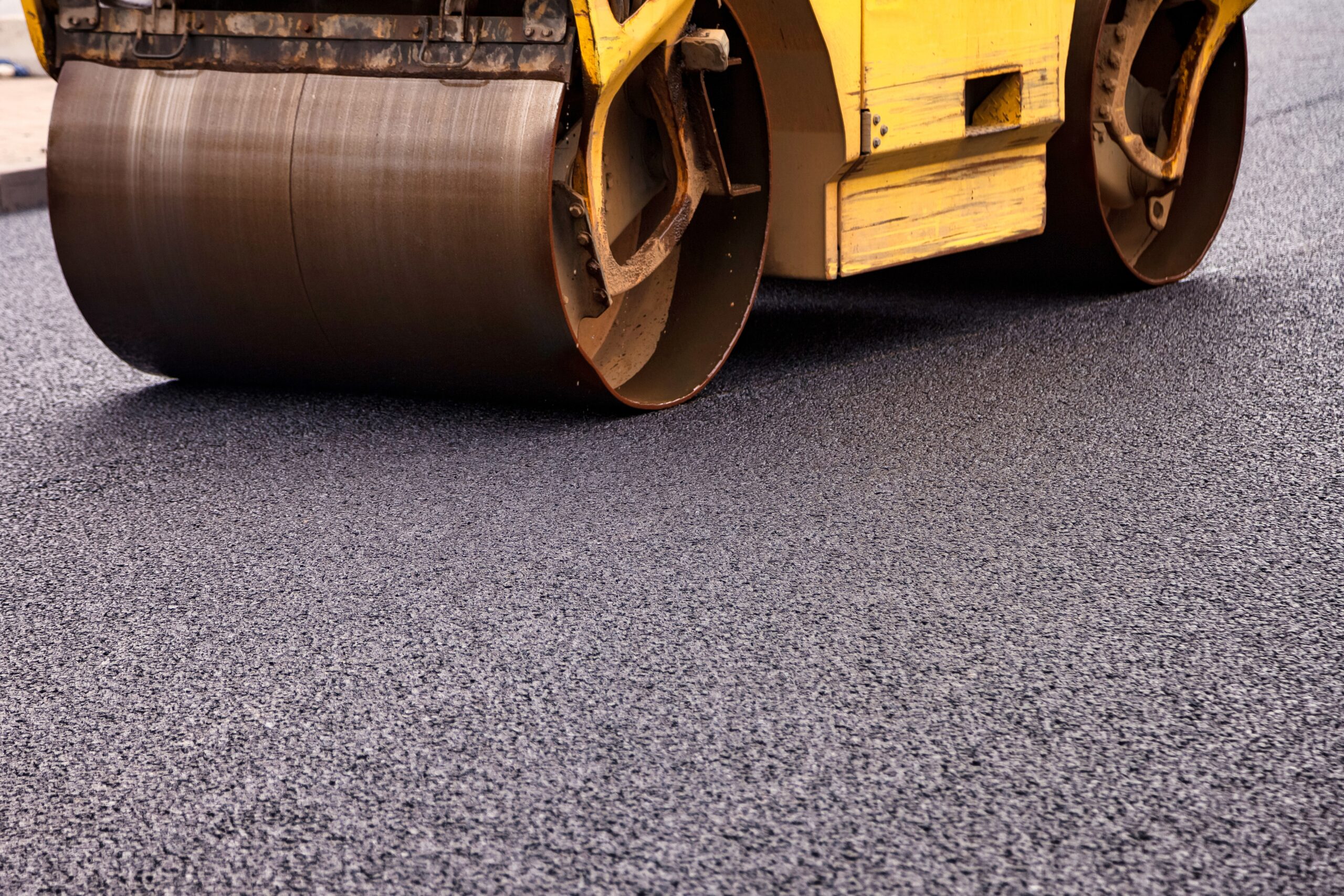 Yellow roller compacting freshly laid asphalt on a driveway, showcasing the process of creating Driveways Greystones