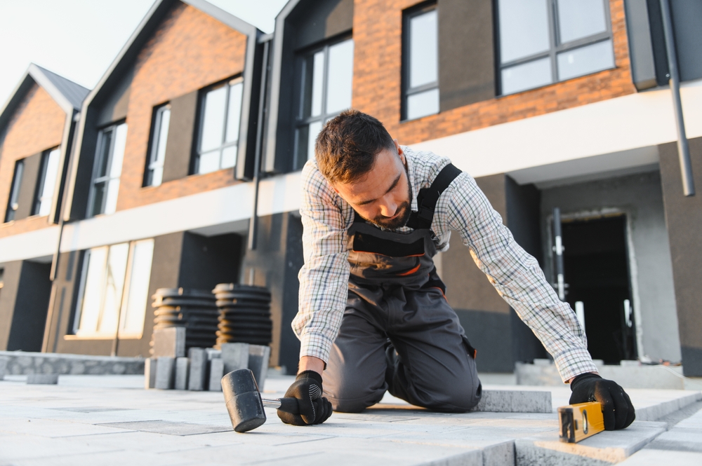 A worker kneels on a patio, using a level and mallet, with modern houses in the background, showcasing Patios Wicklow