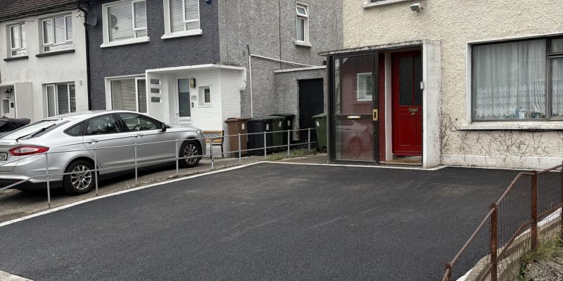 Newly paved black driveway with a white border, adjacent to two residential houses in Wicklow, under a cloudy sky