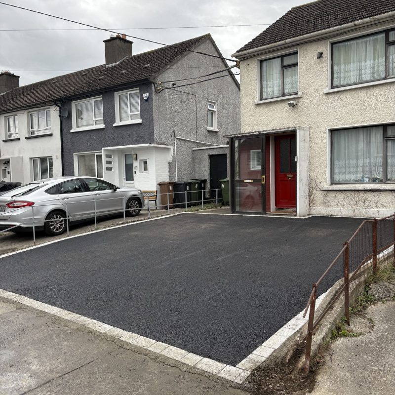 Newly paved black driveway with a white border, adjacent to two residential houses in Wicklow, under a cloudy sky