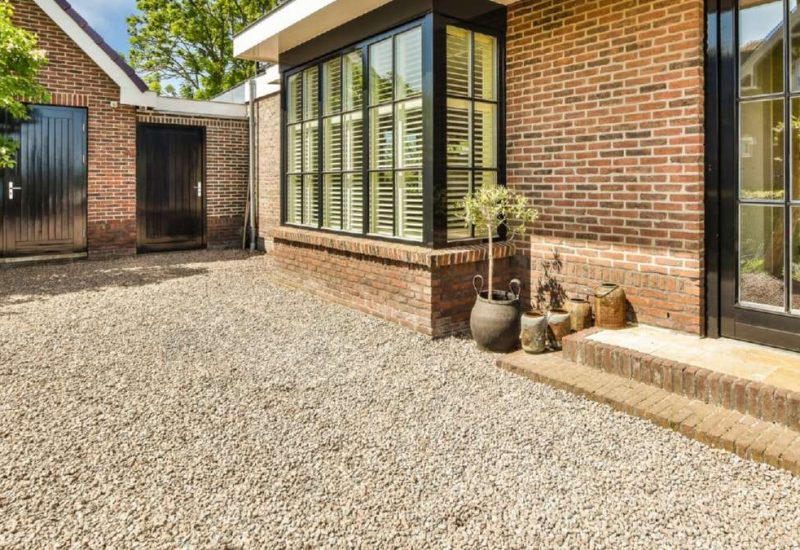 Gravel driveway leads to a modern brick home with large windows, potted plants, and two dark wooden doors in Wicklow